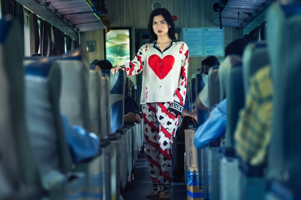 Woman in playing card-print đồ bộ standing in the aisle of a Vietnamese train carriage — The Pyjama Project, Ho Chi Minh City 2025